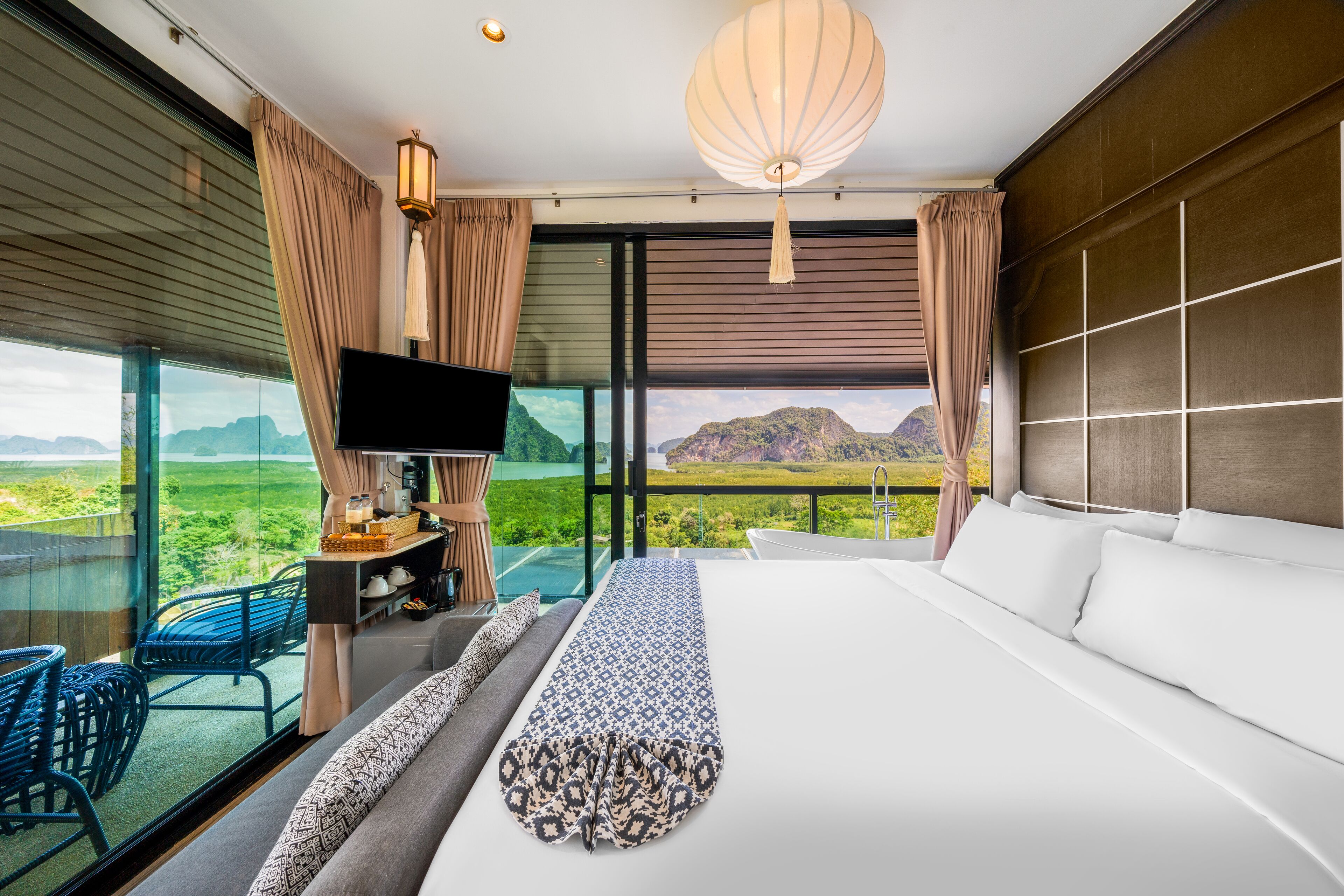 Een moderne hotelkamer met een groot bed, een televisie, een bureau en uitzicht op een bergachtig landschap.