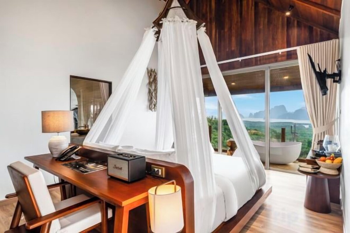 Un dormitorio con cama con dosel, un escritorio con lámpara y vistas al exterior.