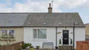 A single-story house with a white exterior, a black front door, and a small front yard with a bench and potted plants.