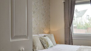 A bedroom with a bed, a window with curtains, and a wall with floral wallpaper.