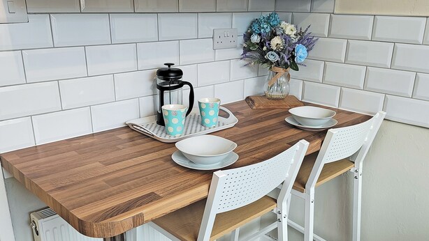 A kitchen with a wooden table, white chairs, a coffee maker, and a vase with flowers.