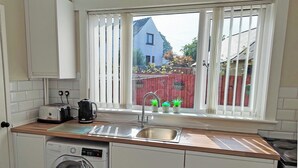 A compact kitchen with a built-in washer, a sink, and a window with blinds.
