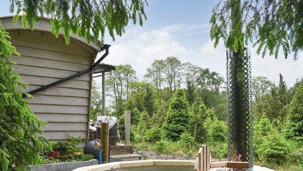 A wooden hot tub in a garden with a house in the background.