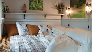 A bedroom with a bed, pillows, a blanket, a small plant, and a painting on the wall.