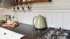A kitchen with a gas stove, a green kettle, a loaf of bread, and hanging mugs.