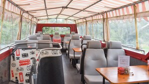 A train carriage with striped canopies, seating, tables, and a view of greenery outside.