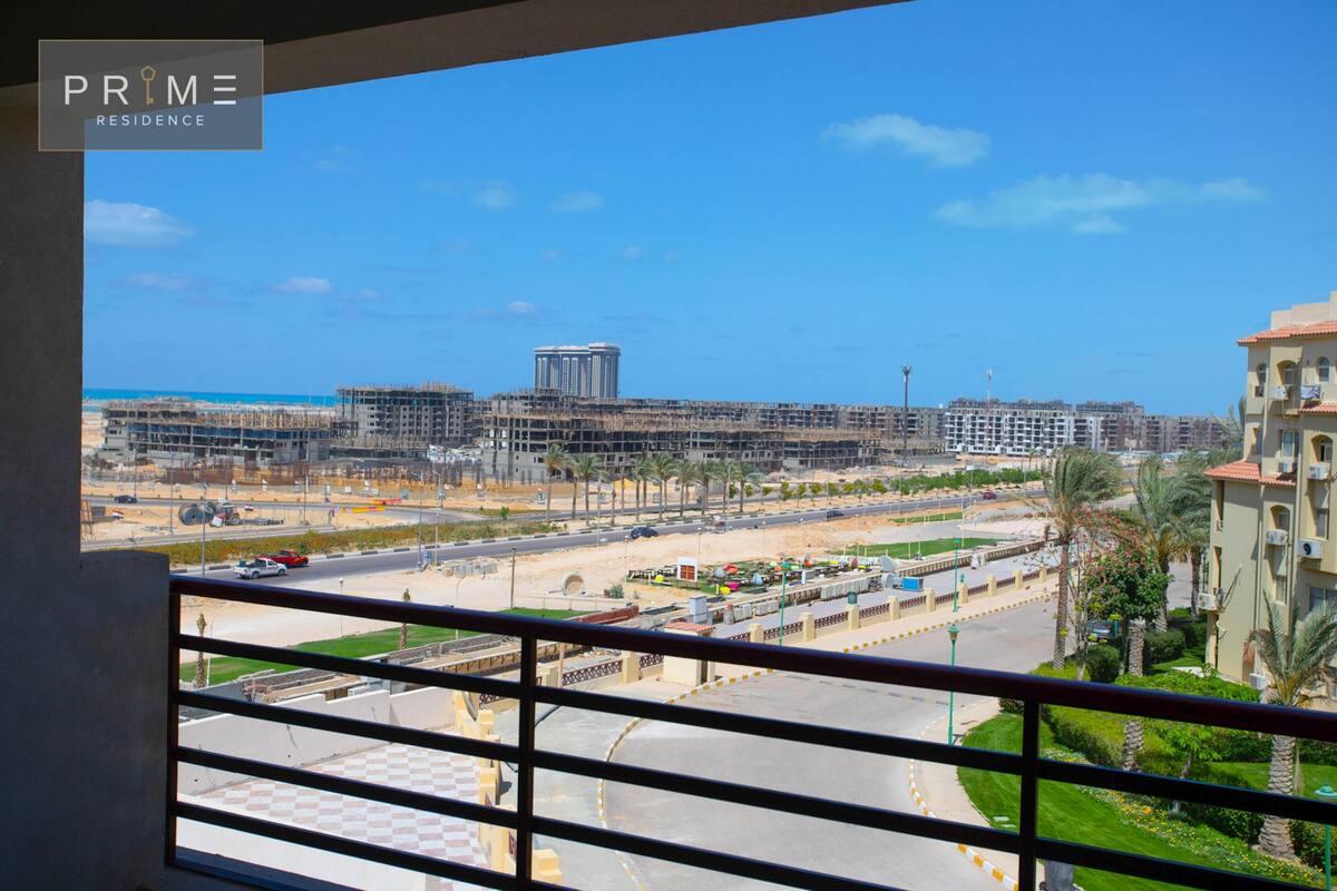 A view from a balcony overlooking a cityscape with buildings, roads, and a beach.