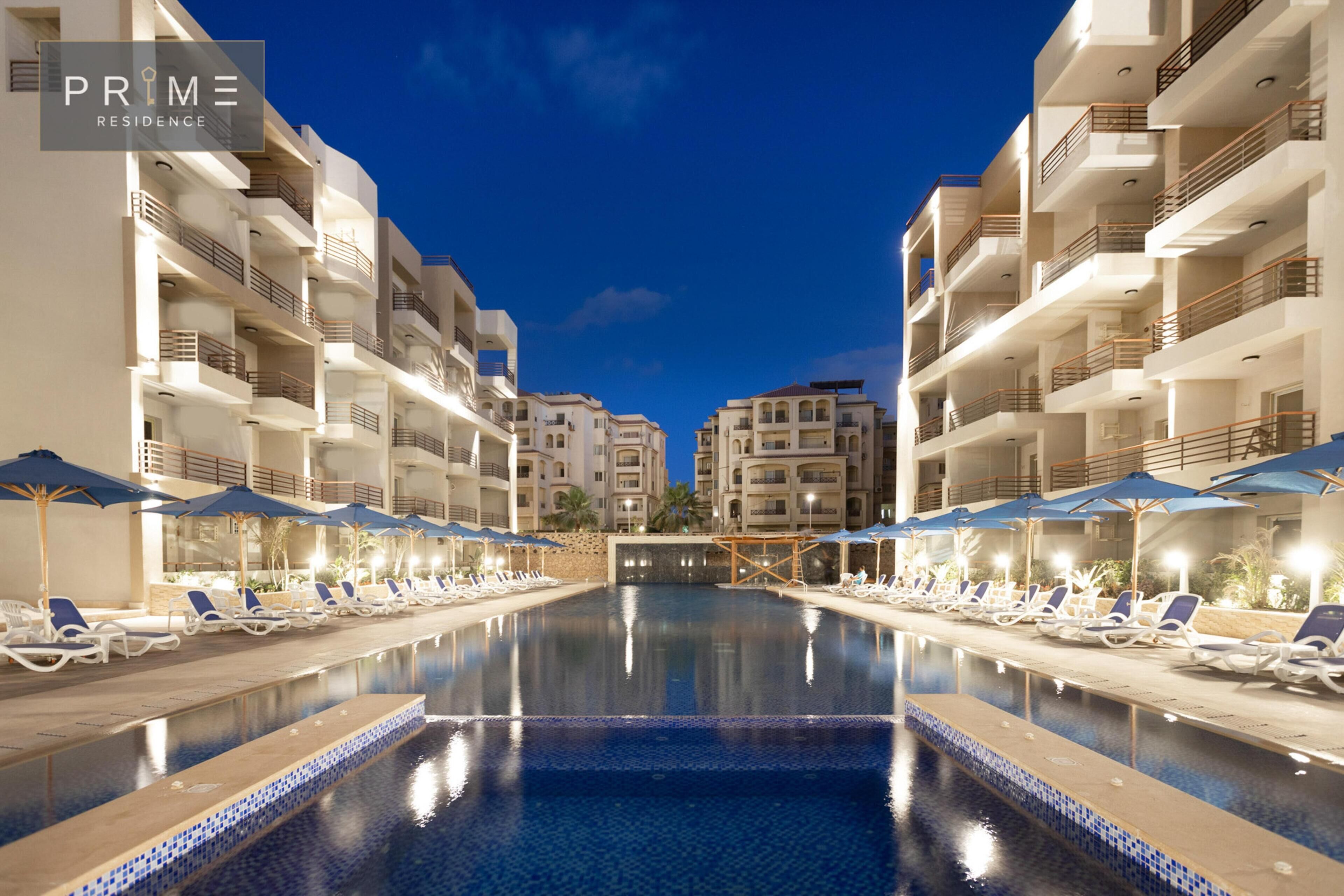 Vista della piscina di un hotel con numerosi balconi, lettini e ombrelloni.