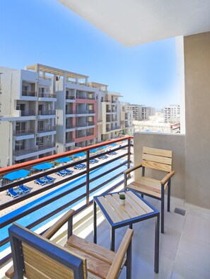 A balcony with a pool view, wooden chairs, and a small table with a plant. - Prime Residence New Alamein (El Alamein)