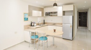 A modern kitchen with white cabinets, a built-in oven, and a refrigerator. There is a dining area with a table and two chairs. - Prime Residence New Alamein (El Alamein)