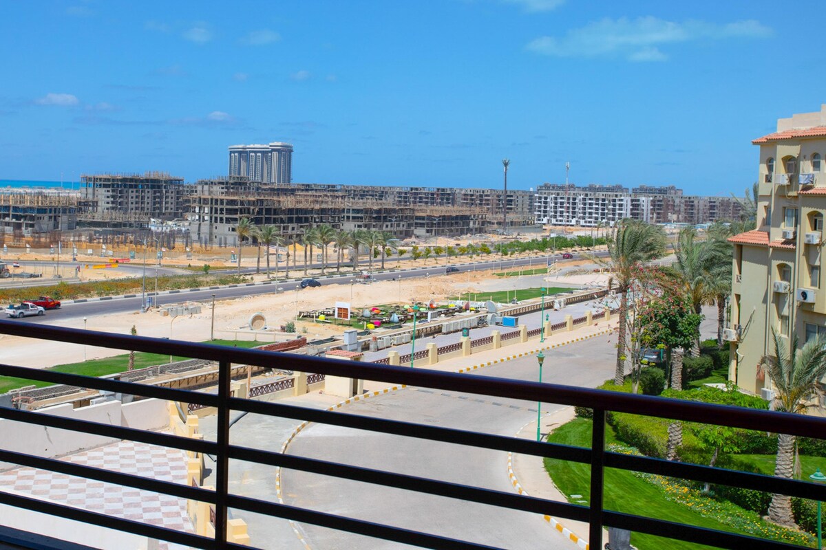 A view from a balcony overlooking a cityscape with buildings, roads, and a beach.