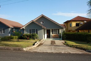 A two-story residential building with a front porch, a small garden, and a clear sky.