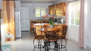 Une cuisine avec des meubles de rangement en bois, une table à manger avec des chaises, un réfrigérateur et une fenêtre avec des rideaux.