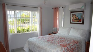 Une chambre avec un grand lit, une fenêtre avec des rideaux, une table de chevet et un climatiseur fixé au mur.
