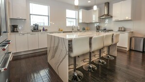 Una cocina moderna con armarios blancos, una isla de mármol y taburetes de bar.