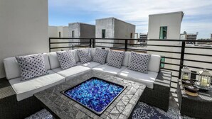 Una terraza en la azotea con un sofá blanco modular, un hogar cuadrado y una barandilla.
