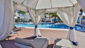Un área junto a la piscina con zona de estar cubierta, piscina y sillas de descanso.