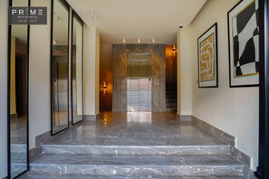 A marble-floored hallway leading to an elevator with framed artwork on the walls. - Prime Residence Sheikh Zayed (Sheikh Zayed City)