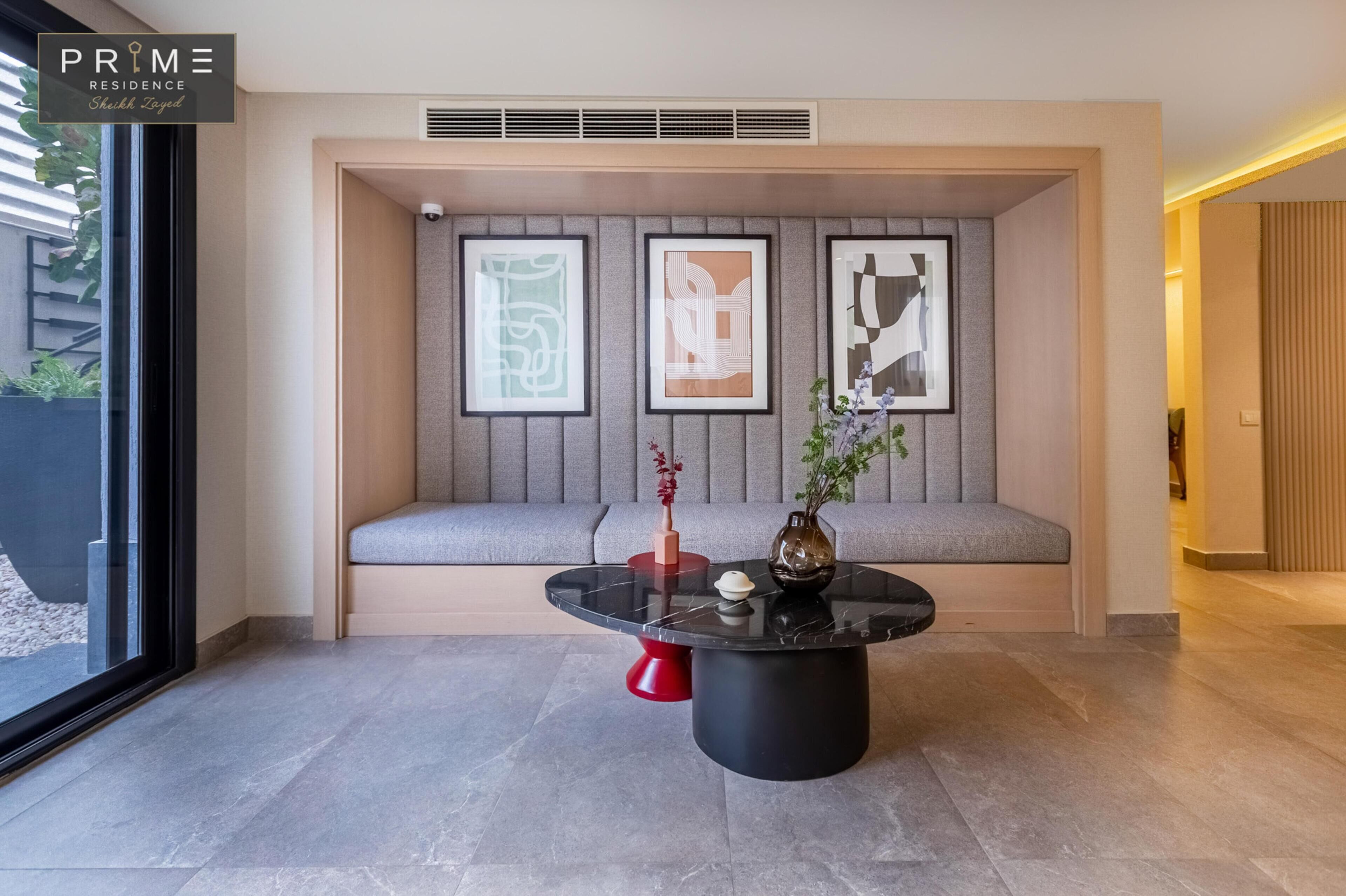 Un intérieur moderne avec une table ronde noire, un banc rembourré de couleur grise et des œuvres d’art abstraites encadrées accrochées au mur.