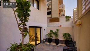 A modern residential building with a glass door entrance, potted plants, and outdoor seating. - Prime Residence Sheikh Zayed (Sheikh Zayed City)