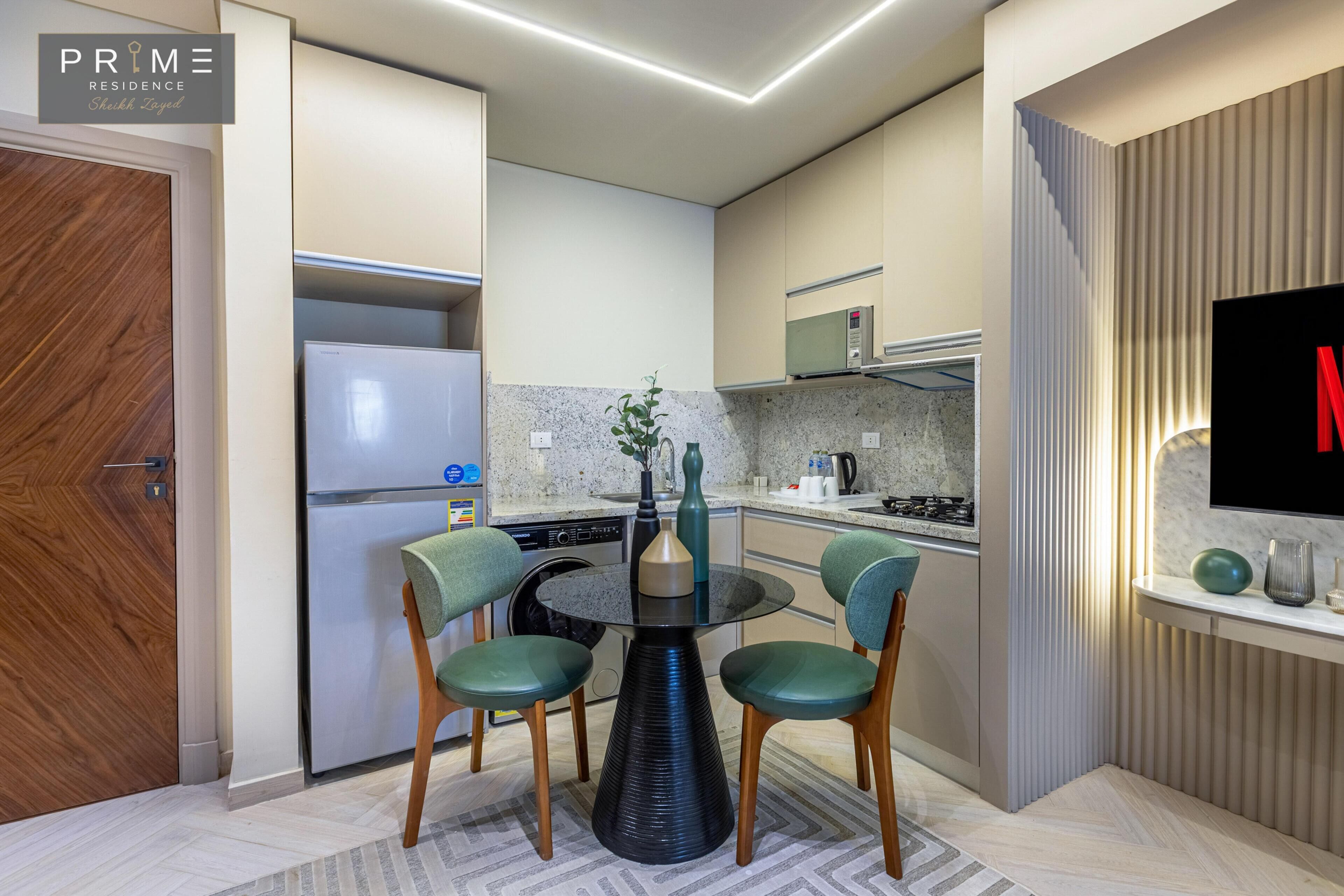 A modern kitchen with a dining area, featuring a built-in oven, microwave, and a flat-screen TV mounted on the wall.