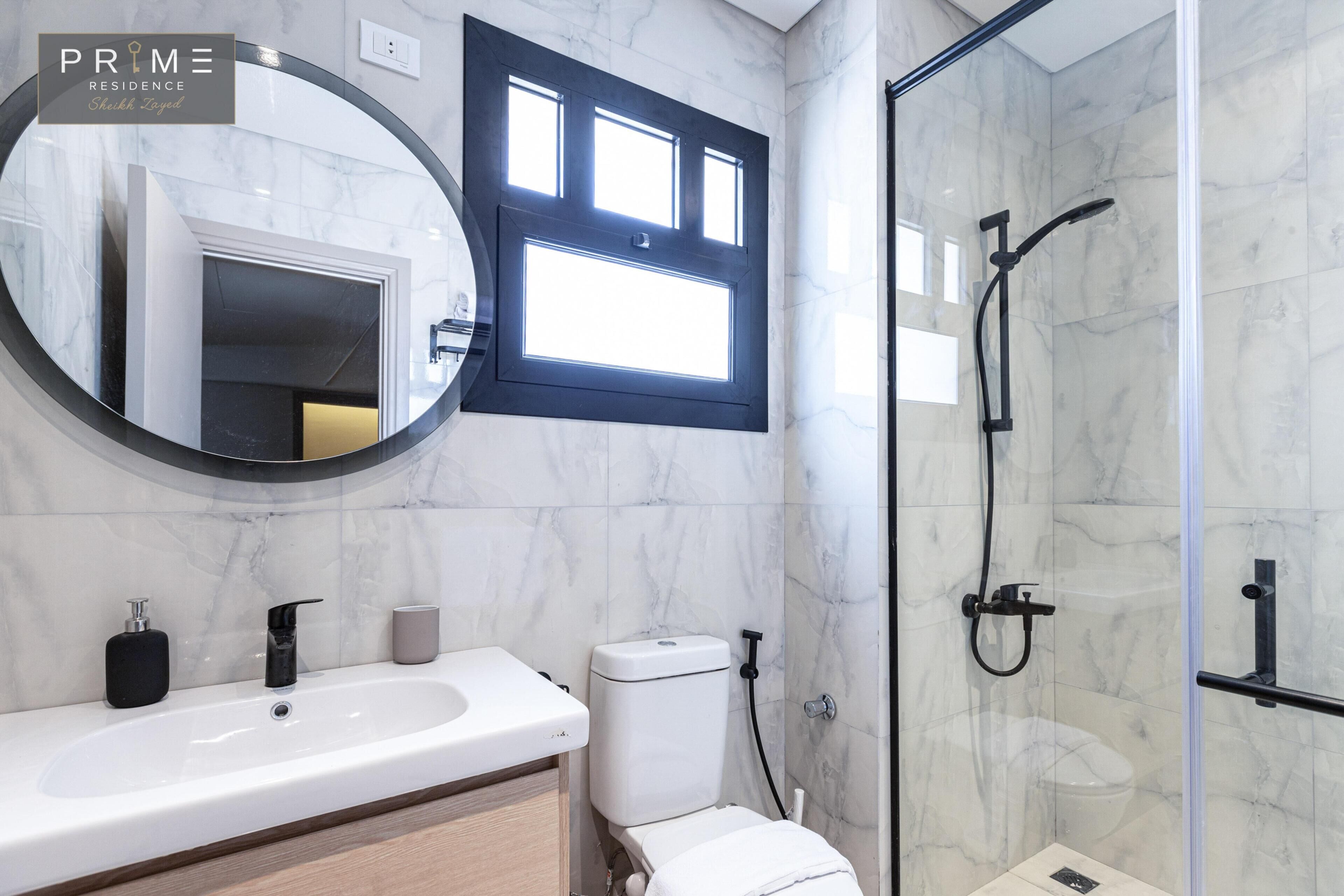 A modern bathroom with a marble sink, a toilet, and a glass-enclosed shower.