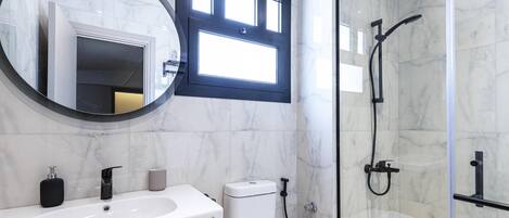 A modern bathroom with a marble sink, a toilet, and a glass-enclosed shower.