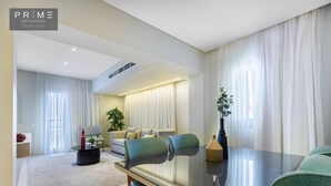 A modern living room with a glass-top dining table, green upholstered chairs, a sofa set, and a large window with sheer curtains. - Prime Residence Sheikh Zayed (Sheikh Zayed City)