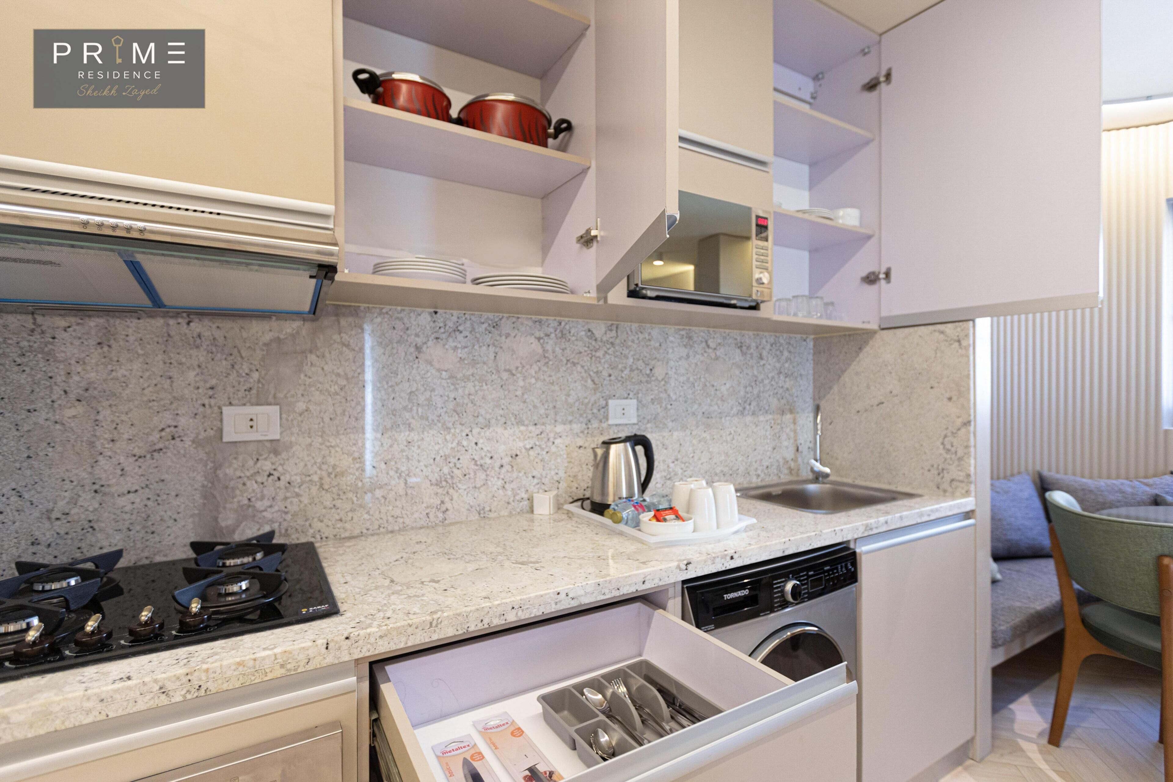 A compact kitchen with a built-in dishwasher, a stove, and a microwave. There are cabinets above the counter and a small sink.