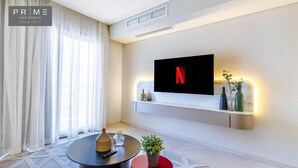 A modern living room with a mounted TV displaying the Netflix logo, a round coffee table, a red accent stool, and a potted plant. - Prime Residence Sheikh Zayed (Sheikh Zayed City)