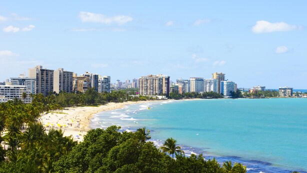 A coastal cityscape with high-rise buildings, a sandy beach, and palm trees.