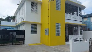 A two-story building with a white and yellow facade, a gated entrance, and a balcony on the upper floor.