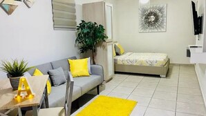 A compact living space with a sofa, a bed, a small table with a plant, and a TV mounted on the wall.