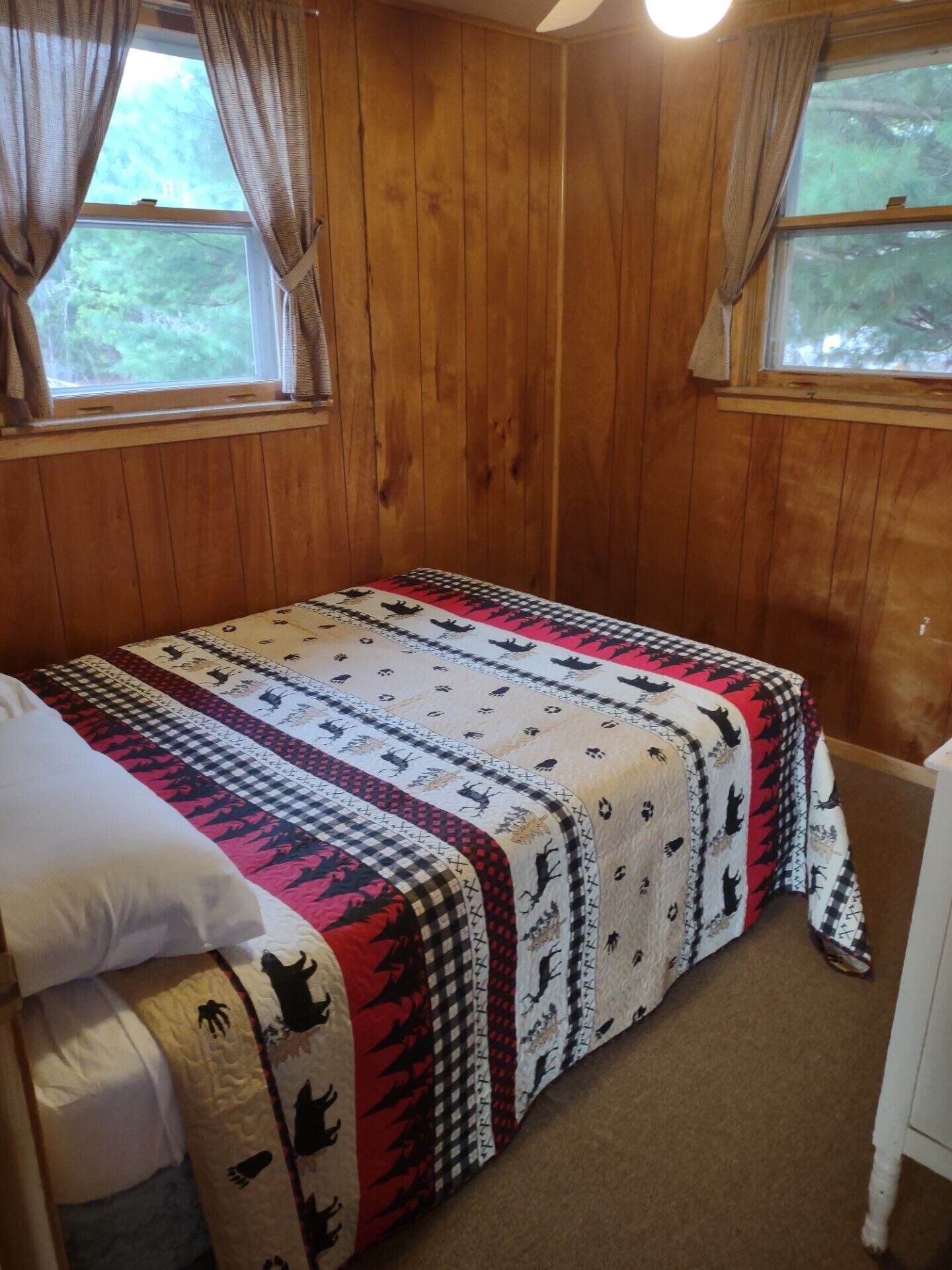 A wooden-paneled room with a bed, a nightstand, and a window with curtains.