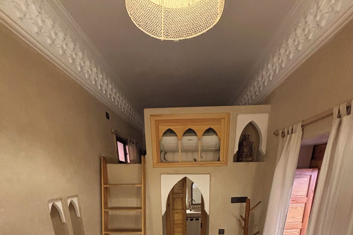 Una habitación con dos camas, una escalera de madera, suelo de baldosas y vistas a un baño a través de un arco.
