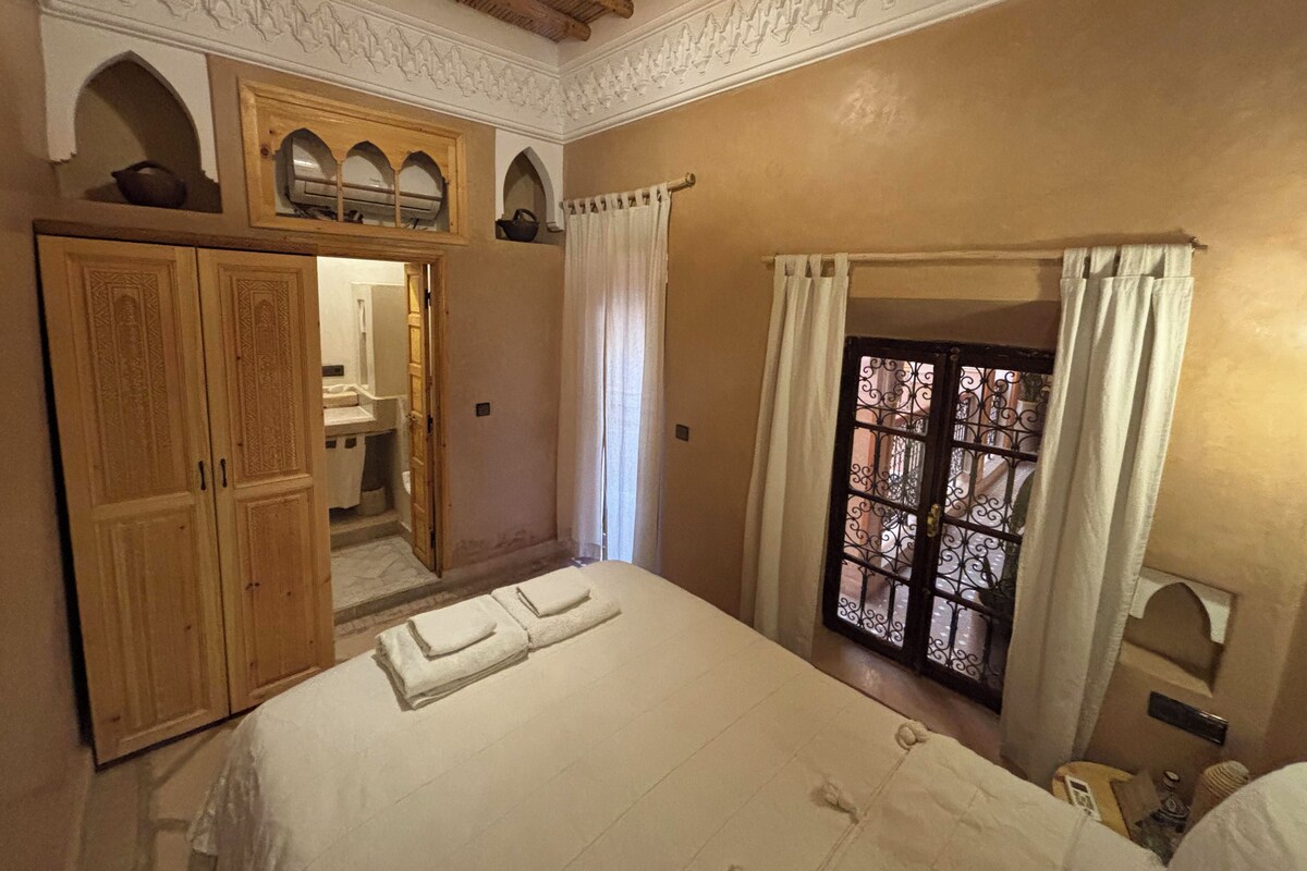 Una habitación con cama, armario, espejo y ventana con cortinas.