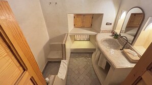 A compact bathroom with a wooden door, a small sink with a mirror, and a tiled floor. - Riad Minami (Marrakech)