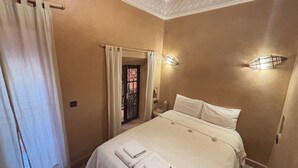 A bedroom with a large bed, two bedside lamps, a window with curtains, and a door leading to another room. - Riad Minami (Marrakech)