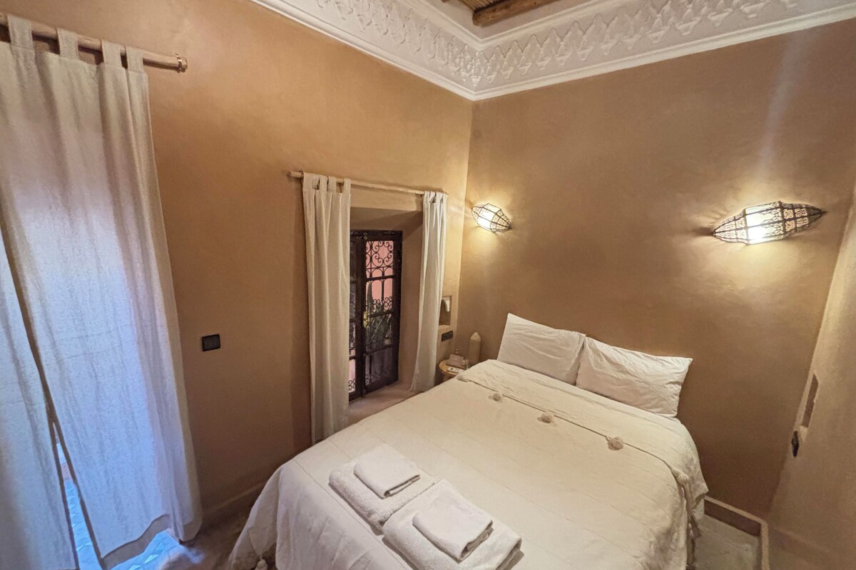 Una camera da letto con un letto, due comodini, una finestra con tende e un soffitto decorato.
