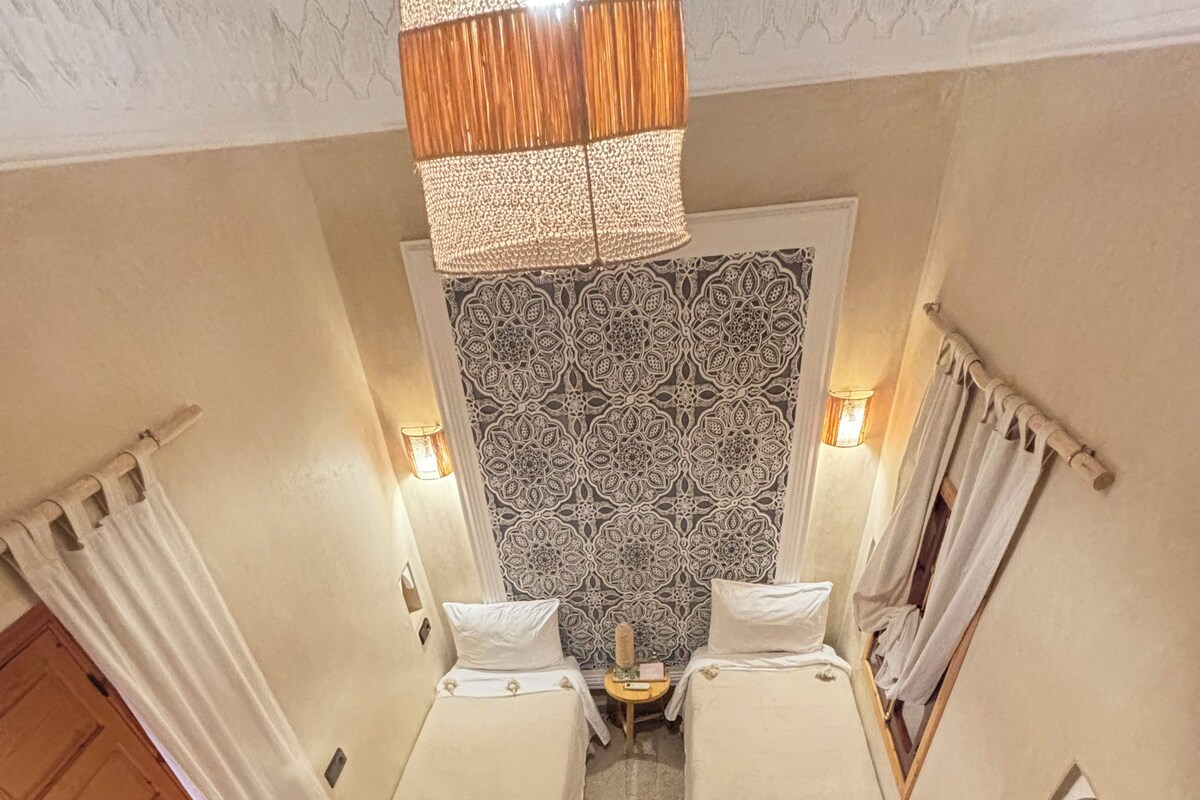 A room with two beds, a patterned wall, a wooden staircase, and a hanging light fixture.