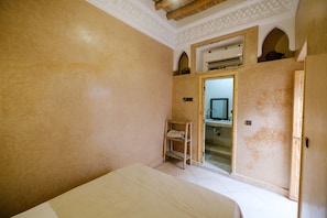 Quarto com cama, uma cadeira de madeira pequena, televisão e porta para um banheiro.