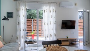Een moderne woonkamer met een bank, een eettafel, een televisie en een schuifpui naar een balkon.