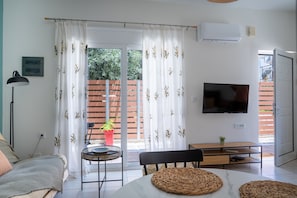 Una sala de estar moderna con un sofá, una mesa de comedor, un televisor y un ventanal corredero que da a un balcón.
