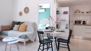 Een modern appartement met een zithoek, bestaande uit een bank, een eettafel met stoelen, en een keuken met witte kasten.