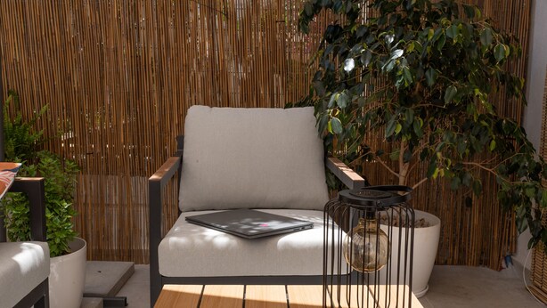 Een modern buitenverblijf met een houten tafel, twee stoelen, een comfortabele bank en een bamboe hek op de achtergrond.