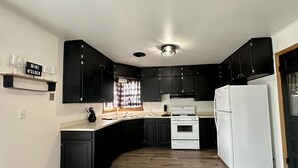Una cocina moderna con armarios negros, un refrigerador blanco y piso de madera.