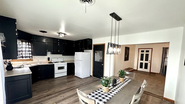 Una cocina moderna con gabinetes negros, un refrigerador blanco y un comedor con mantel a cuadros.
