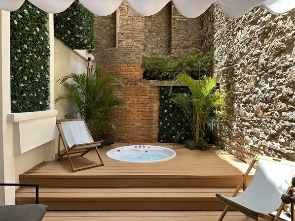 A wooden deck with a hot tub, surrounded by stone walls and lush greenery. - Unique Apartment with Jacuzzi (Ciudad de Panamá)