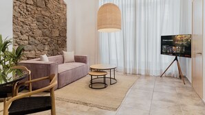 A modern living room with a stone accent wall, a pink sofa, a round coffee table, a hanging light fixture, and a flat-screen TV on a tripod. - Unique Apartment with Jacuzzi (Ciudad de Panamá)