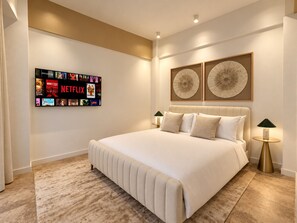 A modern bedroom with a large bed, a wall-mounted TV displaying various shows, two decorative wall art pieces, and a pair of bedside lamps. - Unique Apartment with Jacuzzi (Ciudad de Panamá)